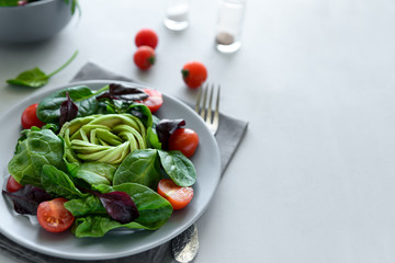 Salad mix with avocado, spinach, tomatoes and beet leaves on gray wooden background. Vegetarian food concept. Selective focus.