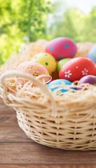 easter, holidays, tradition and object concept - close up of colored eggs in basket on wooden table over green natural background