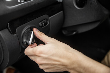 White male hand toggles headlight switch inside the black car.