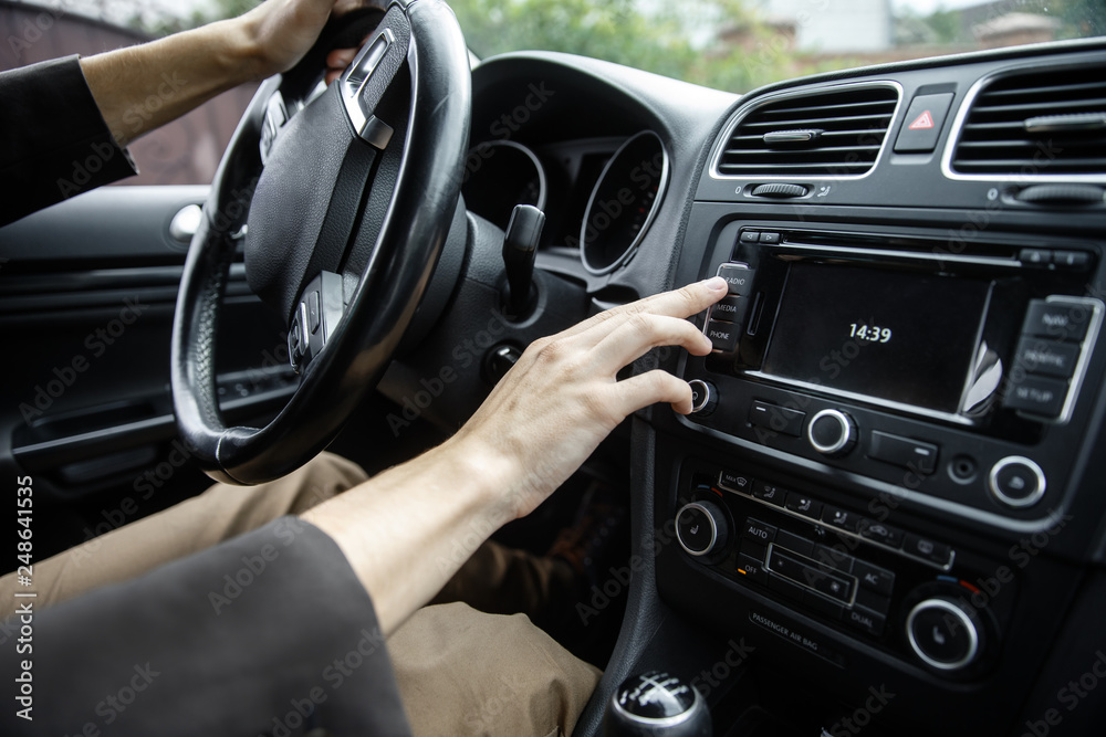 Wall mural white male hand is tuning the radio inside the black car.