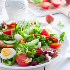 Fresh salad of roasted bacon, cherry tomatoes, quail eggs on a white plate, square