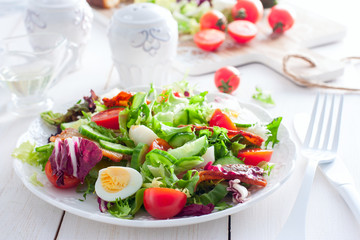 Fresh salad of roasted bacon, cherry tomatoes, quail eggs on a white plate, horizontal