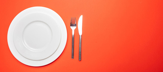 Set of empty white plates and cutlery on red, orange color background, banner