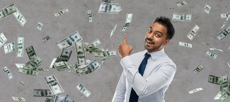 business, office worker and people concept - smiling indian businessman pointing finger at money rain over grey background