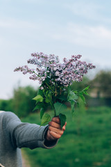 Fototapeta na wymiar bouquet of lilacs in the hands against the backdrop of nature, country road.village, a man gives a bouquet