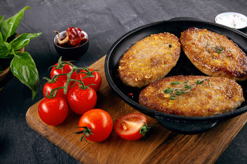 Close up view on burger, cutlets in pan, which stands on cutting board. Fried cutlets with cherry tomato, sauсe and spinach. food menu, recipe concept. Copy space