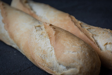 Macro view of freshly baked crunchy baguette bread on dark background. Closeup of crust of bread food background. Natural lighting