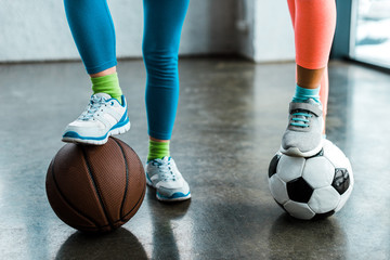 Naklejka premium Cropped view of kids in sneakers posing with balls in gym