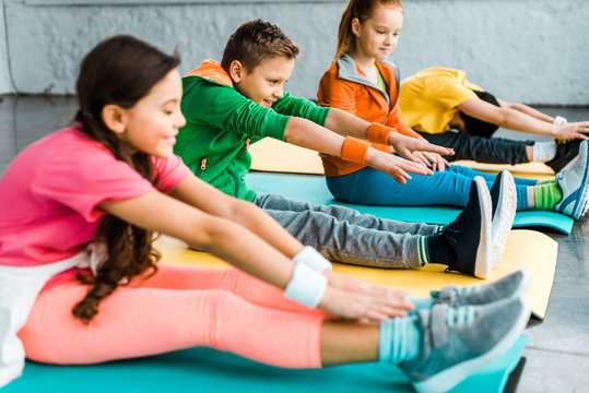 Kids in bright clothes stretching on fitness mats