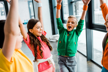 Blissful kids posing with hands up after training in gym