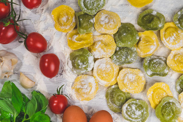 Homemade fresh Italian ravioli pasta on white wood table  with flour, basil, tomatoes,background,top view.