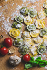 Homemade fresh Italian ravioli pasta on wood table  with flour, basil,tomatoes,background,top view.