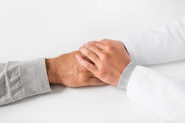 medicine, healthcare and old age concept - close up of young doctor holding senior patient hand