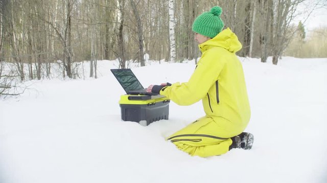 Woman Ecologist in sportswear working on the laptop in winter forest. Steadicam shot