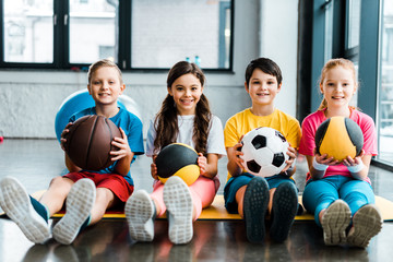 Preteen kids sitting on fitness mat with balls