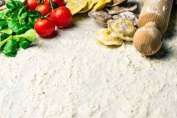 Homemade fresh Italian ravioli pasta on white wood table  with flour, basil, tomatoes,background,top view.