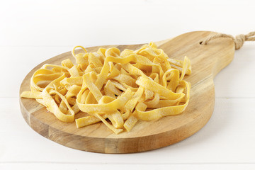 Homemade tagliatelle on chopping board on wooden white background