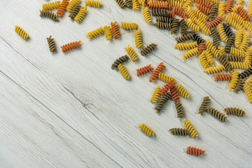 Raw uncooked three-colored Fusilli  on white wood table.