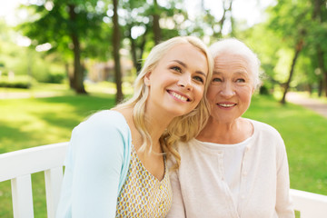Naklejka premium family, generation and people concept - happy smiling young daughter with senior mother sitting on park bench a