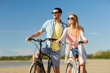 people, leisure and lifestyle concept - happy young couple riding bicycles on beach