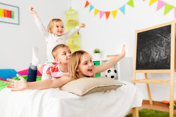 childhood, leisure and family concept - happy little kids having fun in bed at home