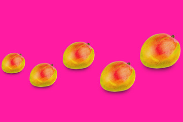 Horizontal row of whole ripe mango from small to large on pink background