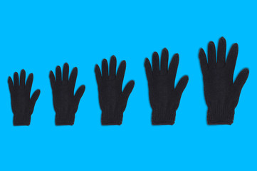 Horizontal row of black warm woolen gloves from small to large on blue background. Top view