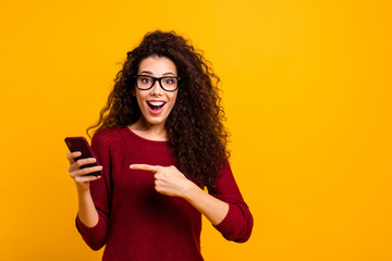 Portrait of her she nice cute lovely attractive cheerful amazed wavy-haired lady holding in hands pointing at cell incredible omg isolated over bright vivid shine orange background