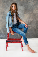 Girl model sitting on a red chair, gray background