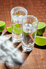 Tequila silver shots with lime slices and salt on wooden board