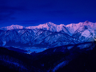 峠からのアルプス山脈を見渡す、夜明け前のブルー、谷間から町並みの街灯り、アルプス山脈は雪景色で朝焼前のピンク色に染る。