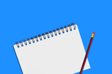 One paper notepad with spiral binder and blank sheets near wooden pencil lies of blue office table. Top view. Concept of business or education. Copy space for your text