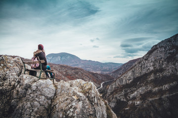 Girl sitting on the bench on the cliff of the canyon with amazing view