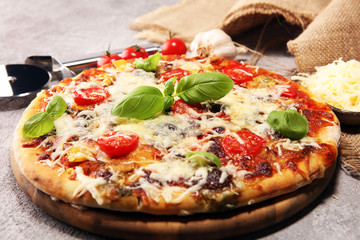 Vegetarian Italian pizza with melted cheese, red tomatoes and green basil on a table decorated by cheese, tomato and cherry tomatoes