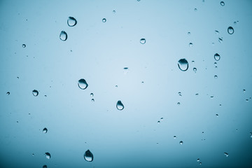 Window glass with drops of rain. Atmospheric mint blue aqua light background with raindrops. Azure droplets close up. Detailed transparent aquamarine texture in macro with copy space. Rainy weather.