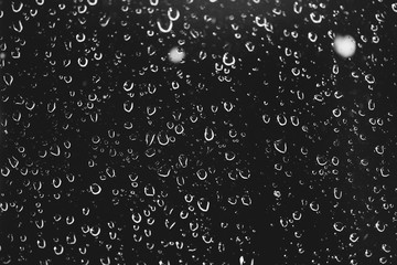 Dirty window glass with drops of rain. Atmospheric monochrome dark background with raindrops. Droplets and stains close up. Detailed transparent texture in macro with copy space. Night rainy weather.