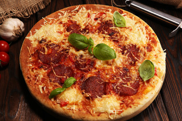 Italian pizza with salami, peperoni - with melted cheese, red tomatoes and green basil on a table decorated by cheese, tomato and cherry tomatoes