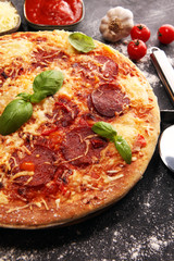 Italian pizza with salami, peperoni - with melted cheese, red tomatoes and green basil on a table decorated by cheese, tomato and cherry tomatoes