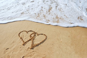 Valentine's day concept, two heart shape drawing on sand beach with ocean background.