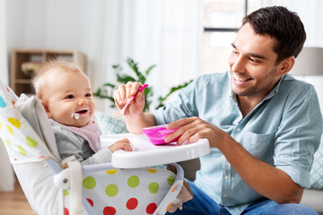 family, food, eating and people concept - happy father feeding little baby daughter sitting in...