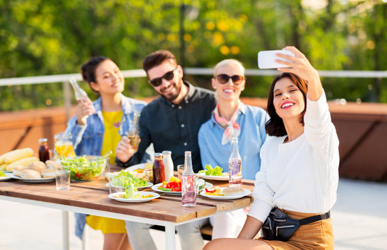 leisure and people concept - happy friends with non alcoholic drinks having dinner party on rooftop in summer and taking selfie by smartphone
