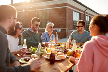 leisure and people concept - happy friends with drinks having dinner or barbecue party on rooftop