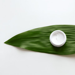 Facial cream Flat lay photo White jar with skincare product on a white background with green decorative leaf Template for posters and banners