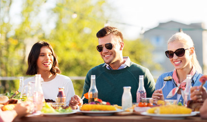 leisure and people concept - happy friends eating and drinking at rooftop party in summer