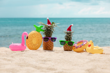 Family of funny attractive pineapples in stylish sunglasses on the sand against turquoise sea. Wearing christmas hats. Christmas and new year vacation concept on tropical beach. Family holiday. Bright