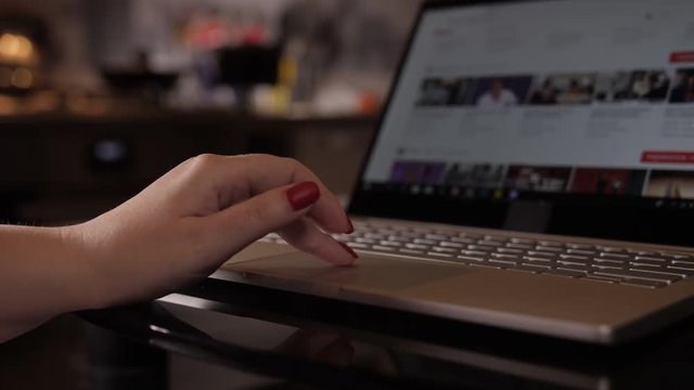 woman hand with manicure scrolls news feed on a laptop, close up