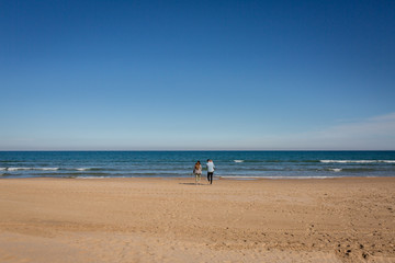 Fototapeta na wymiar Young family walking in empty beach Gandia, Spain