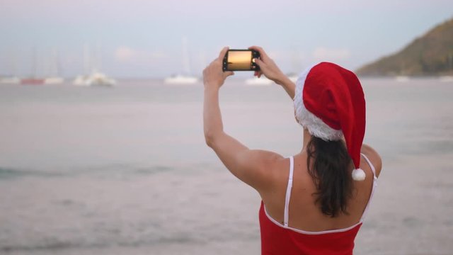 Smiling modern woman in red swimsuit taking photo with smartphone mobile camera on the seashore at sunrise