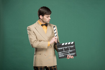 handsome man in vintage clothes holding film clapperboard isolated on green