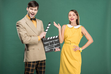 handsome man in vintage clothes holding film clapperboard while beautiful woman gesturing with hand isolated on green